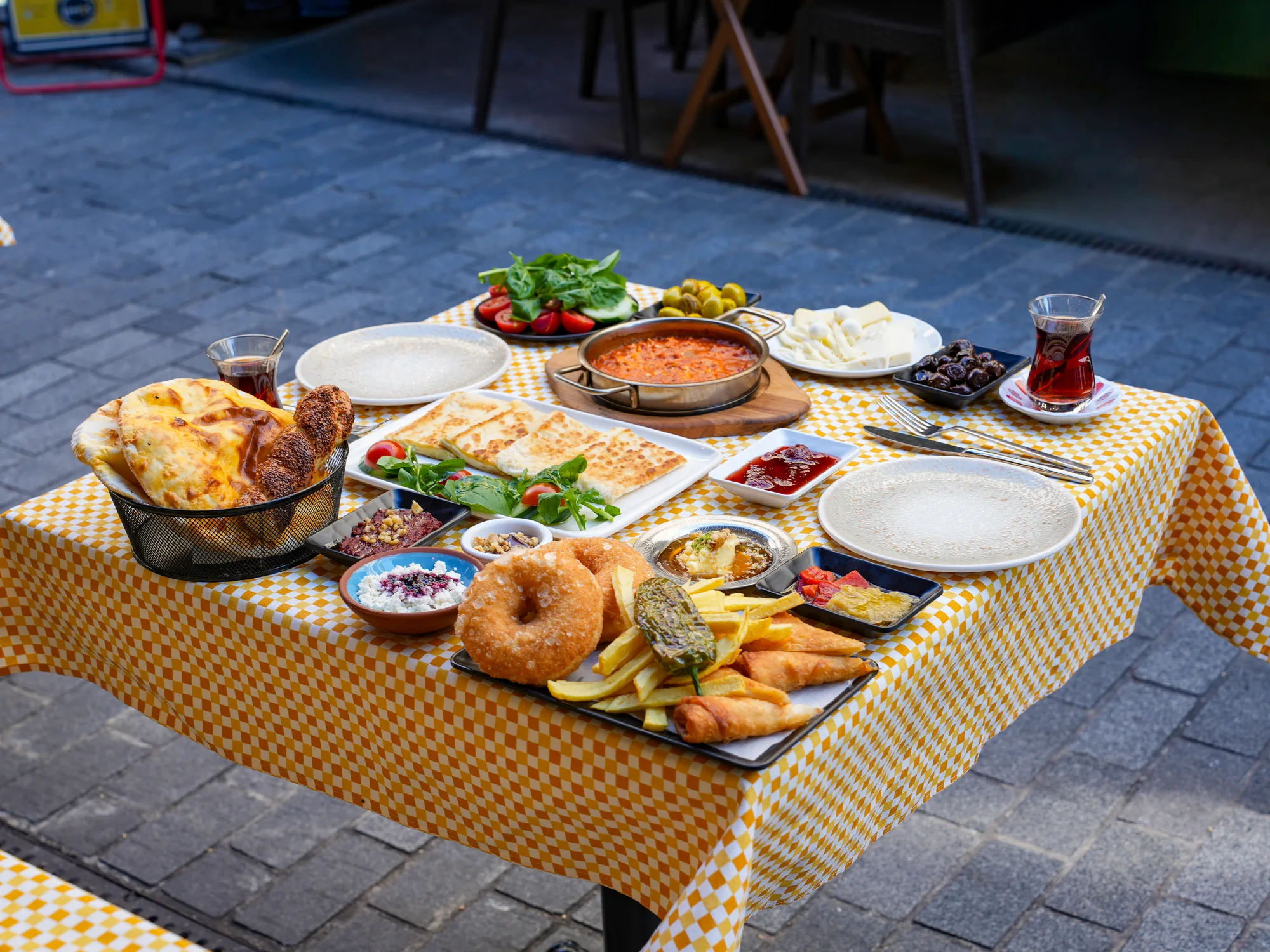 Limos'ta sokak masasında serpme kahvaltı: menemen tavası, sıcak pişi, taze peynirler, sigara böreği ve tavşankanı çaylar